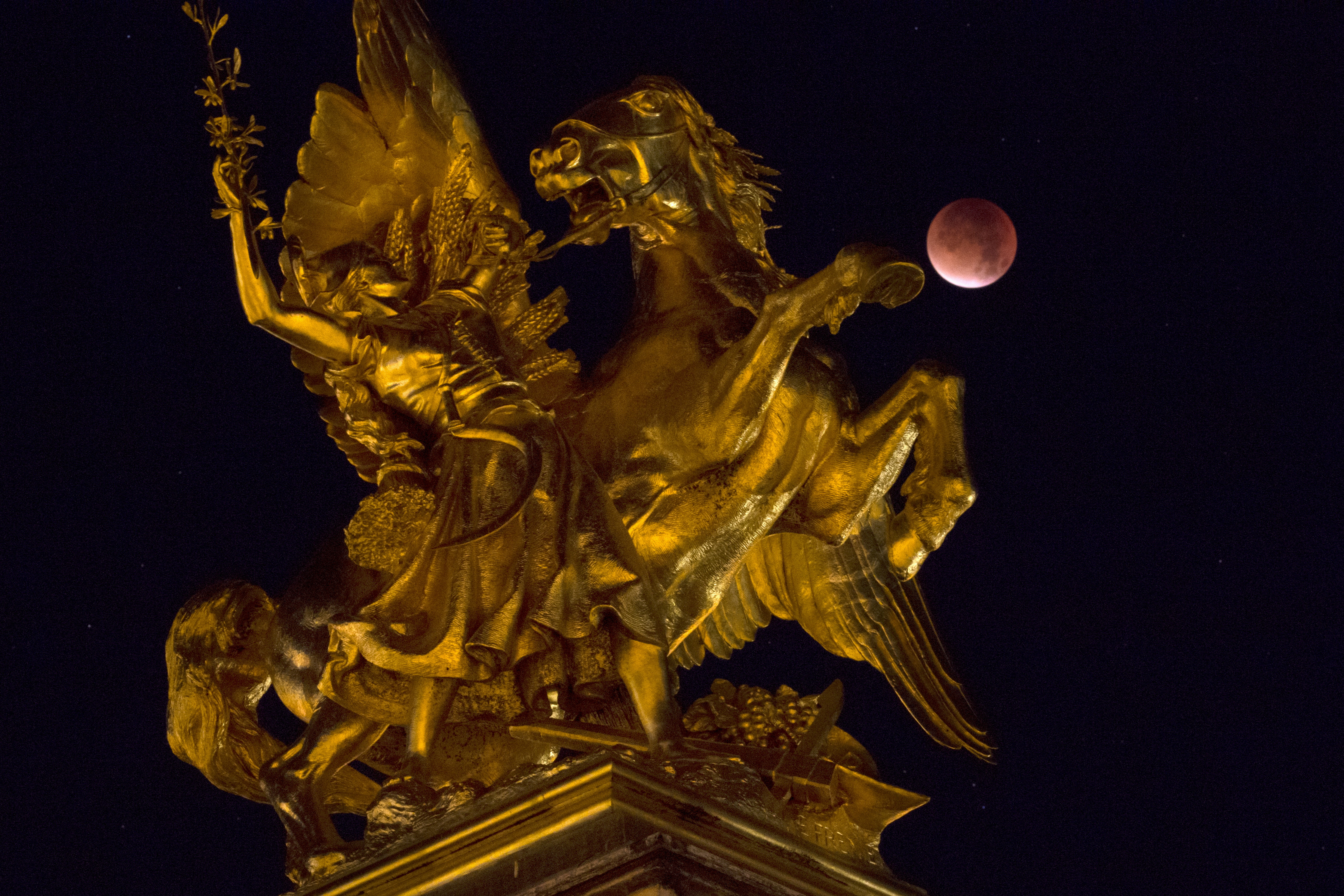 The Moon appears next to a statue on the Alexander III bridge in Paris